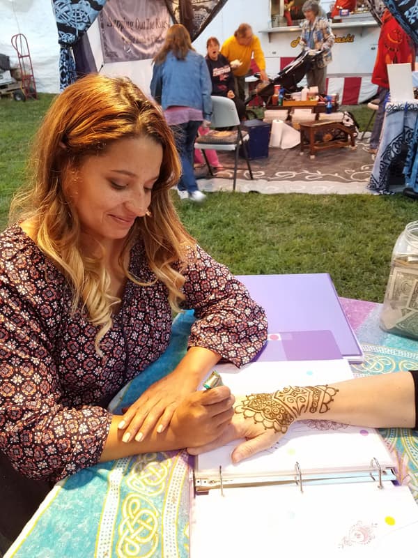 Henna Haven artist applying a custom henna design to a guest at an outdoor festival