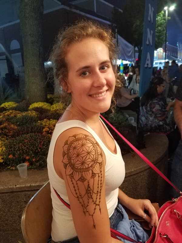 Guest at an evening festival with a henna dreamcatcher design on her shoulder