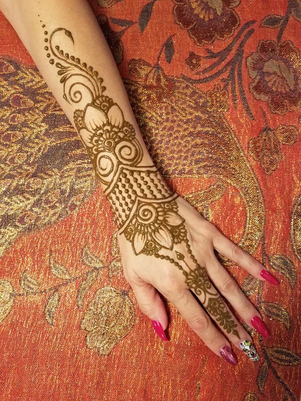 Elaborate floral henna sleeve flowing from the forearm down to the fingertips