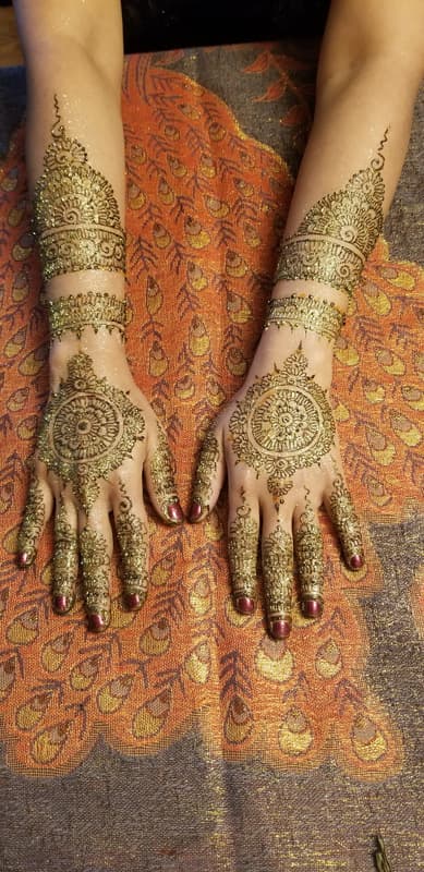 Matching bridal henna medallions and cuffs on both hands, resting on an orange sari