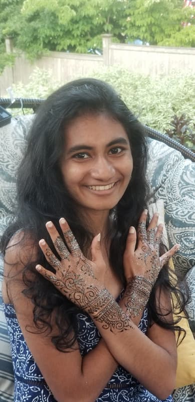 Smiling guest showing off glittered henna covering both hands and forearms